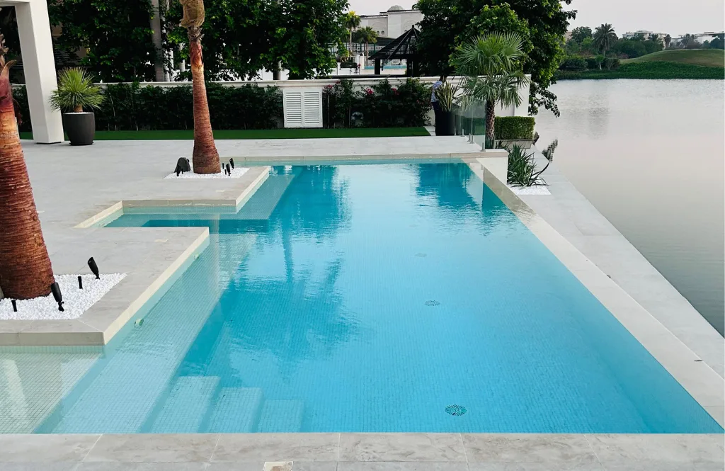 Waterfront swimming pool framed by palm trees and pale stone paving