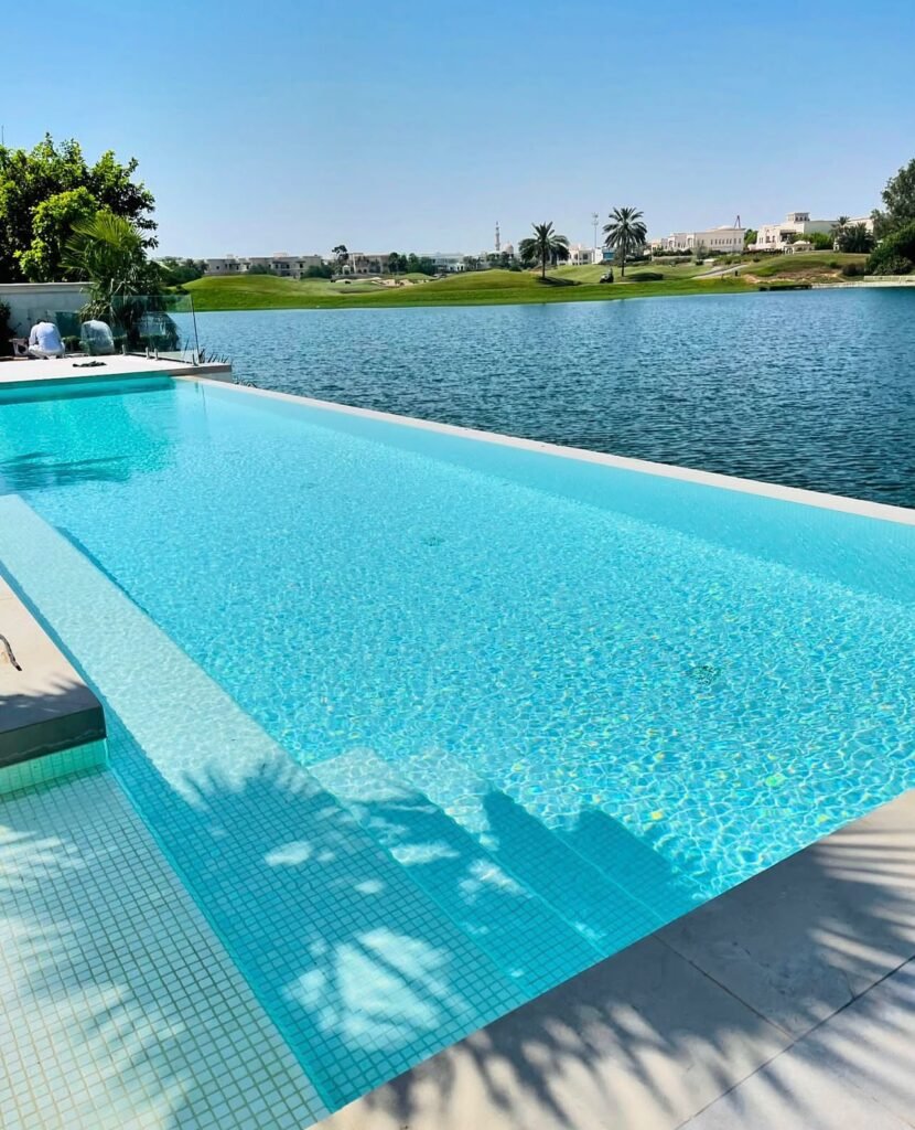 A tiled swimming pool with a broad shallow ledge, paved surroundings and an open view across the lake.
