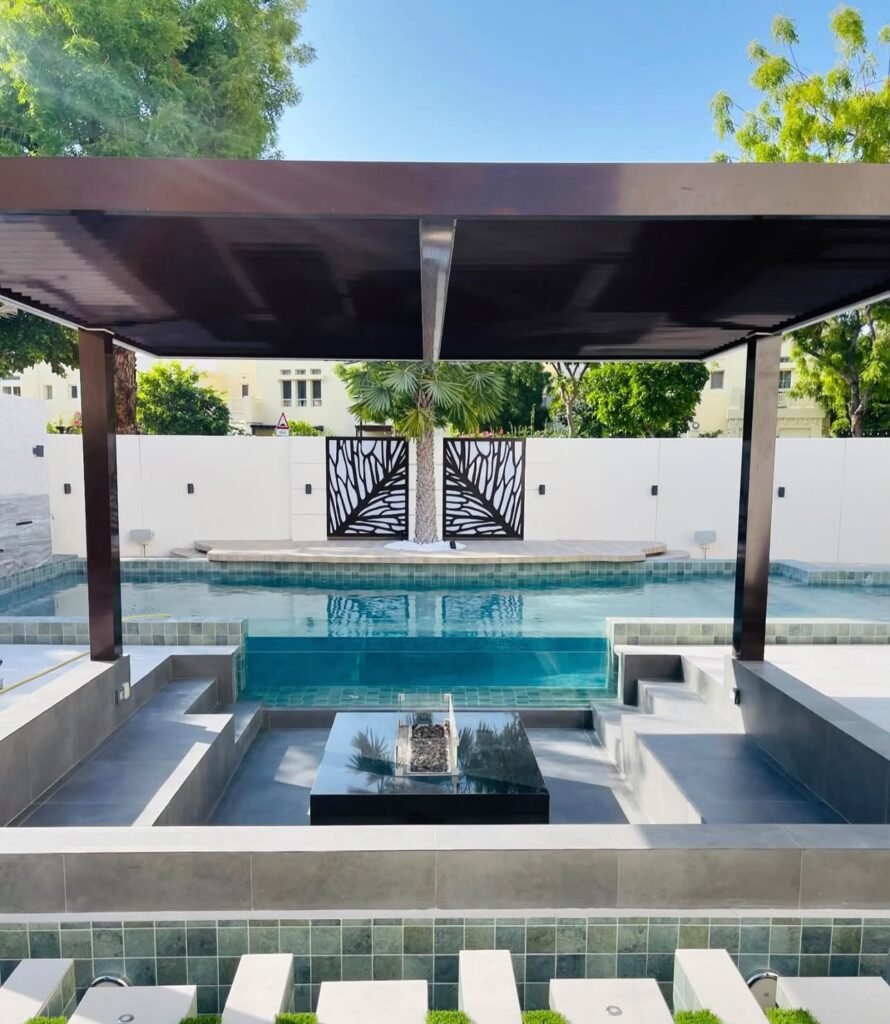 A sunken seating area beneath a pergola, with built-in benches and a central table beside the swimming pool.