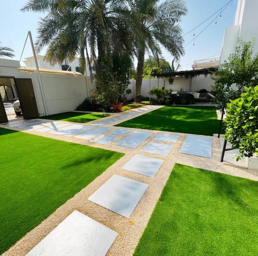 A garden lawn divided by pale stepping-stone paths, with gravel borders and established palms.