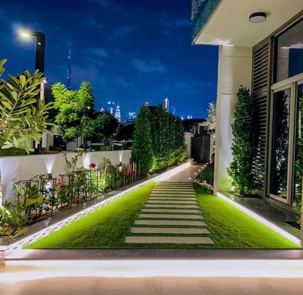 A stepping-stone pathway through lawn strips, with illuminated edges and planting along the garden boundary.