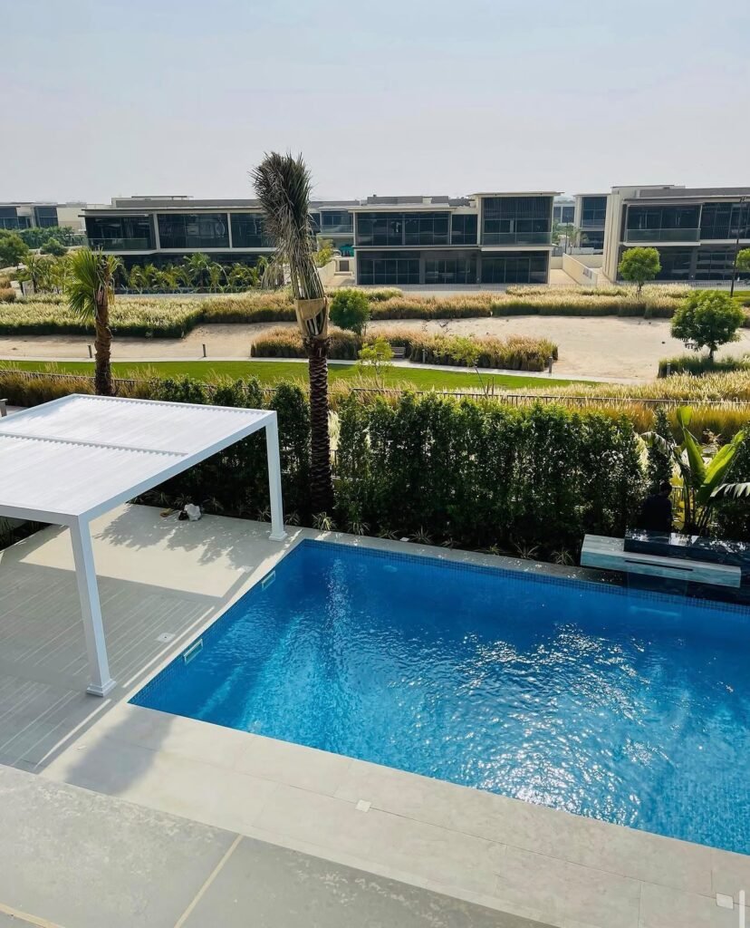 A swimming pool beside a pale paved terrace and shaded seating, with planted screening along the boundary.