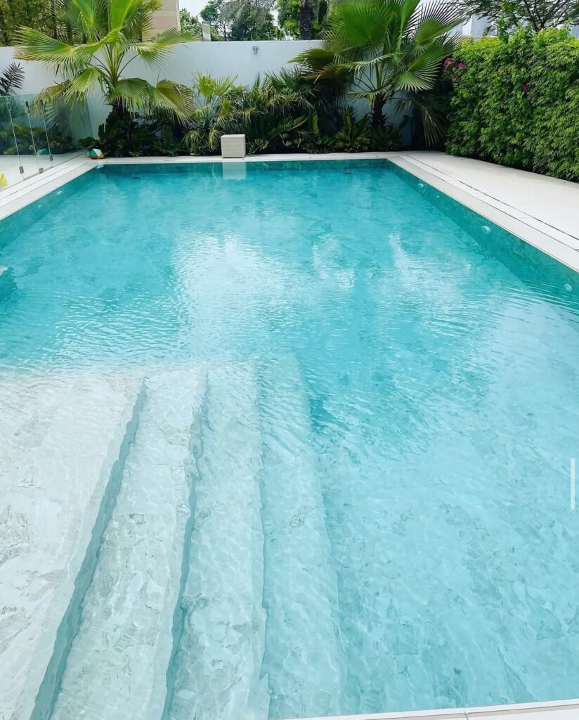 Broad submerged entry steps leading into a tiled swimming pool, with pale coping and dense planting beyond.