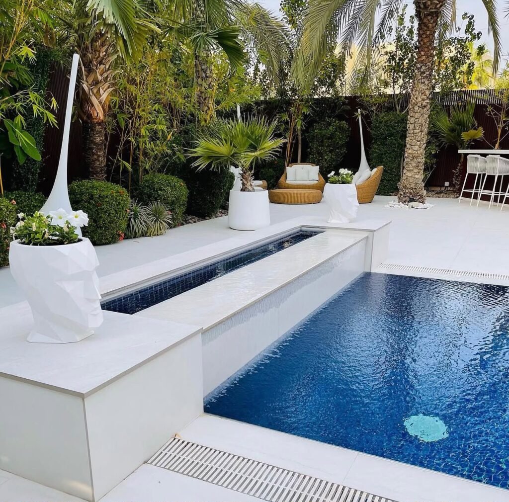 A swimming pool with a raised tiled water channel, white poolside finishes and planting around the terrace.